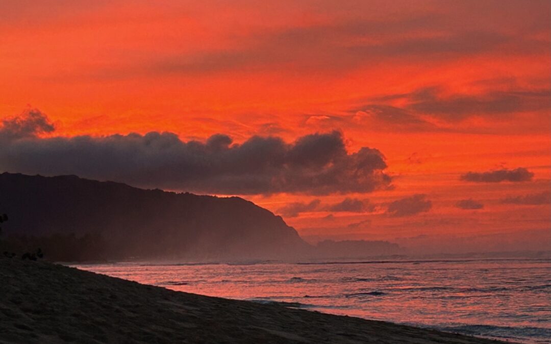 Vibrant Hawaii North Shore sunset sky over a sandy beach with the sun setting behind a distant hill, perfect for ocean adventure seekers.